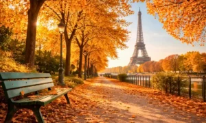 Les Feuilles mortes lyrics — bright autumn Paris scene with golden leaves covering a tree-lined path, green bench, and Eiffel Tower in the background under warm sunlight