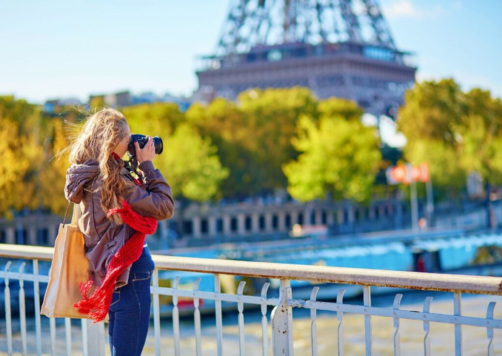 Woman in Paris taking picture on bridge in front of Eiffel tower.